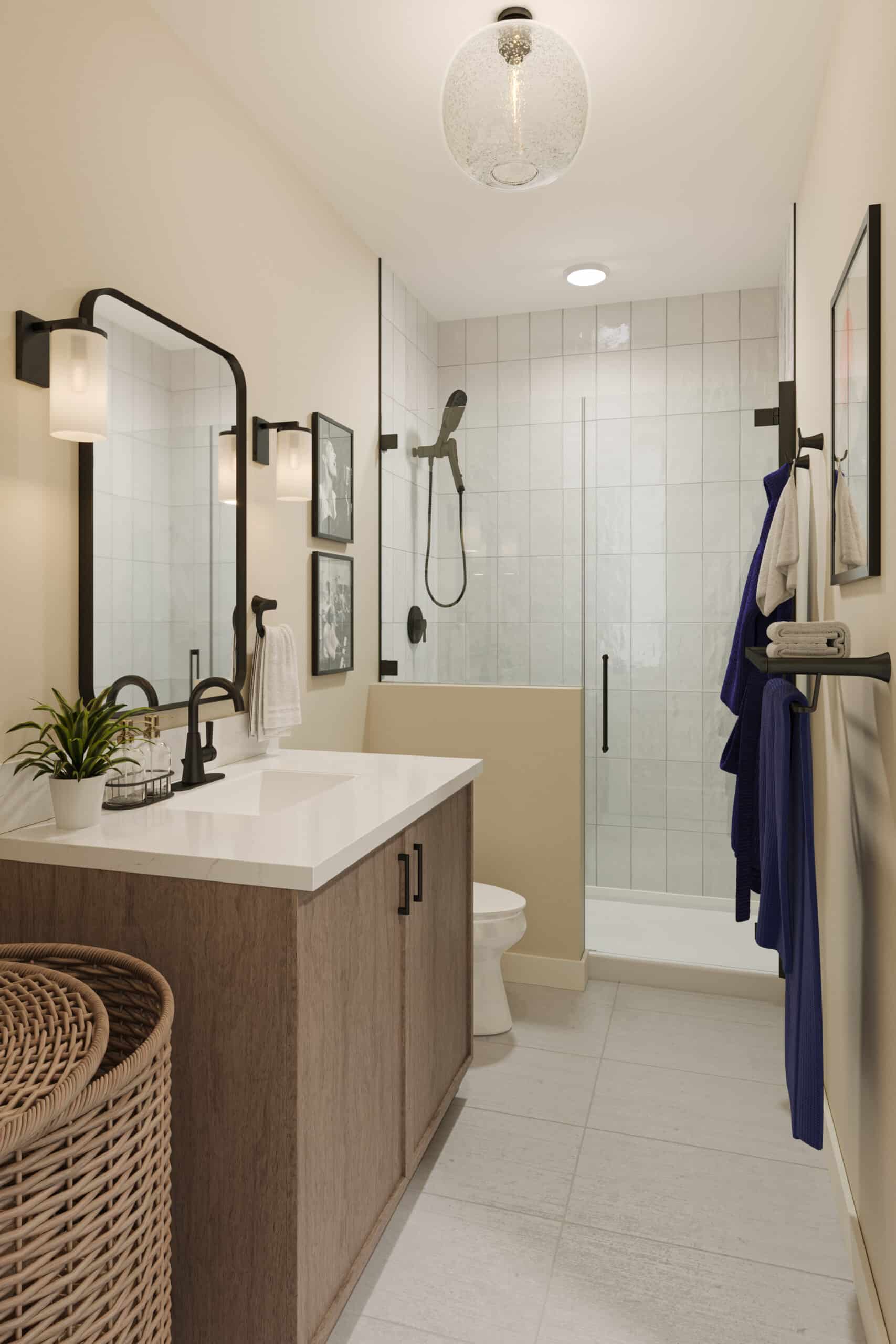 Small modern bathroom with a wooden vanity, white countertop and sink, glass-enclosed shower with black fixtures, wall mirror and sconces, wicker laundry basket, and towels hanging on a rack.