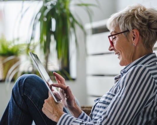 a woman is sitting with knees propped up using a tablet device.